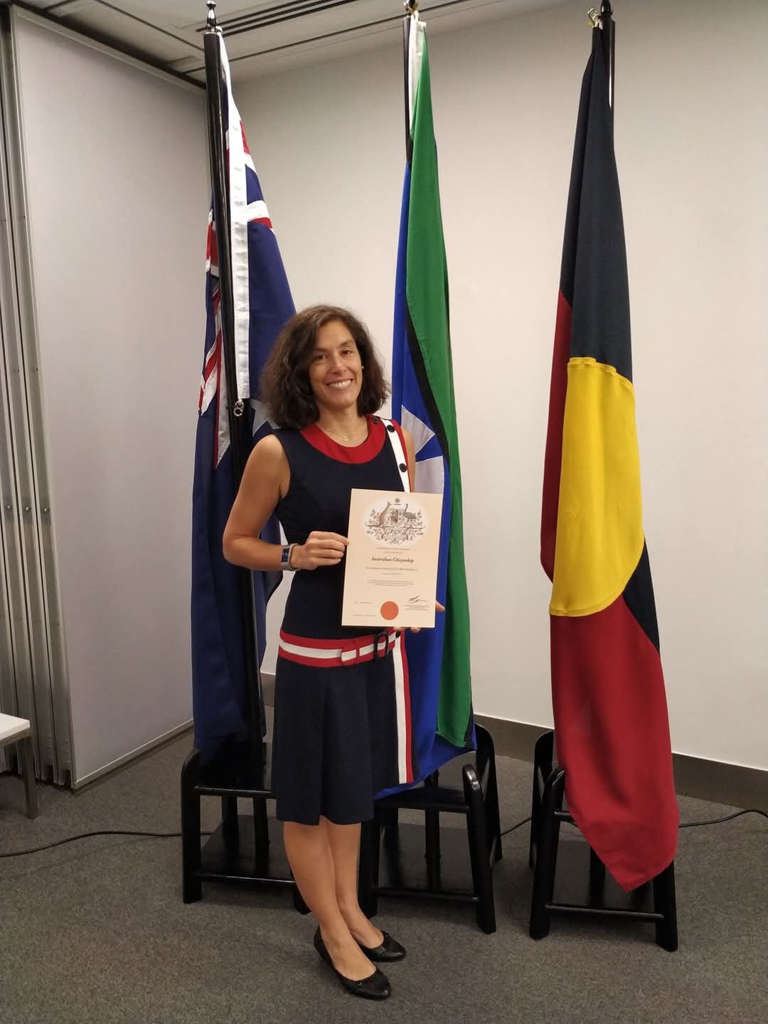 Eva stands proudly in front of the Australian, Australian Aboriginal, and Torres Strait Islander flags as a newly minted Australian citizen.